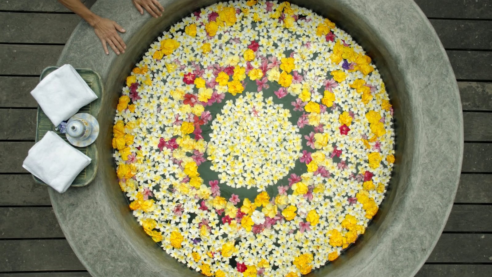 A carved stone tub seen from above, its water covered in a spiral of frangipani, hibiscus and marigold petals.