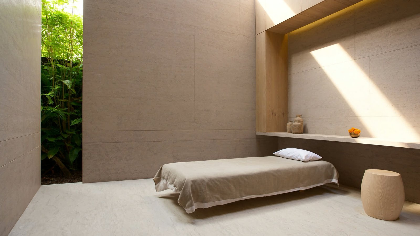 An empty minimalist spa treatment room in warm micro-cement with low afternoon light from a courtyard.