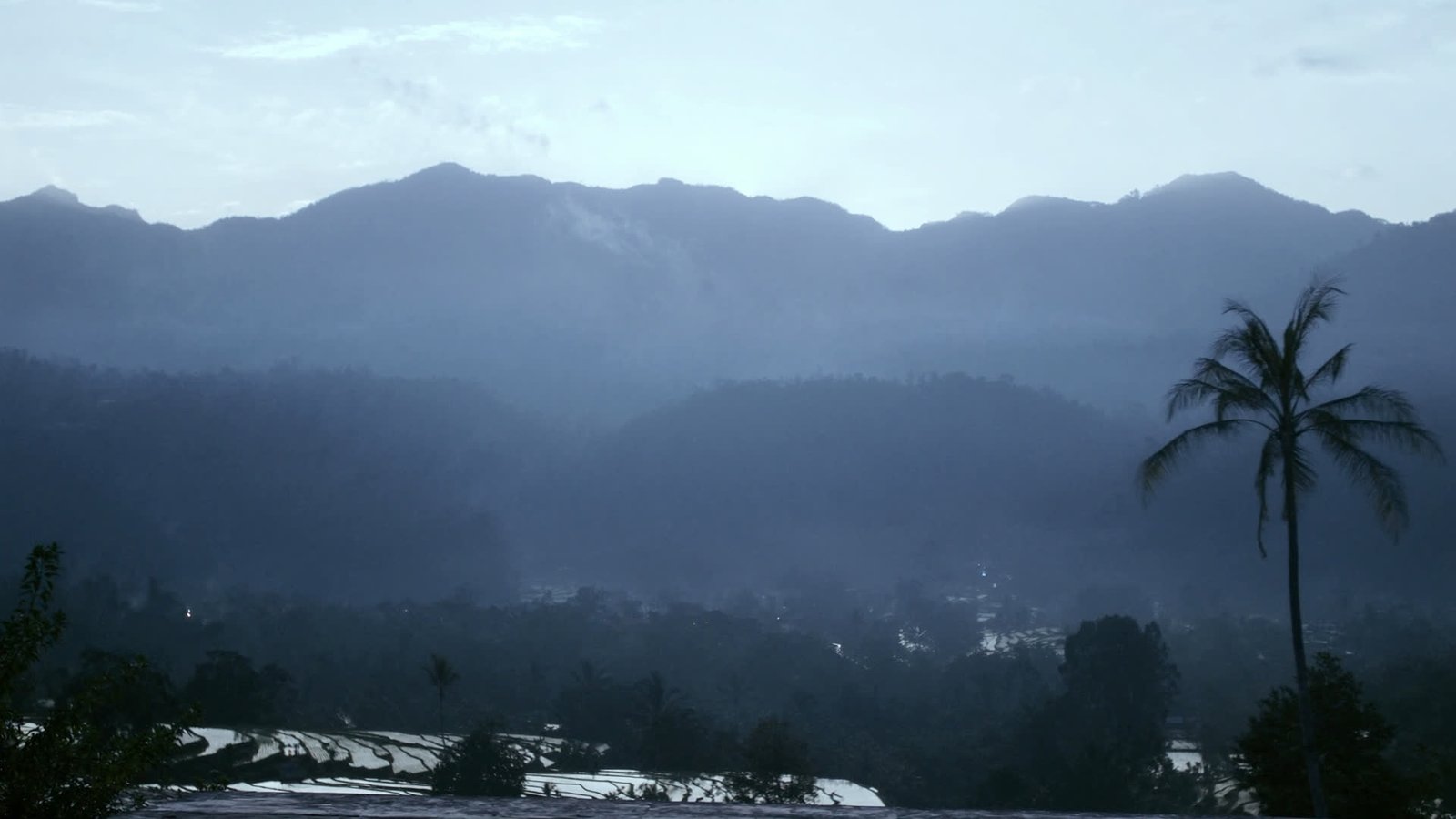 Ridgelines and rice terraces in the Balinese highlands before sunrise, still in cool blue mist.
