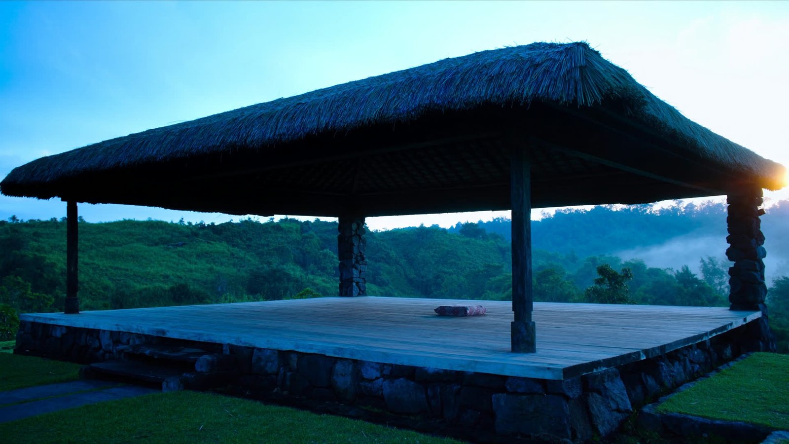 An empty open air meditation pavilion of teak and thatch in the Bali highlands at first light.