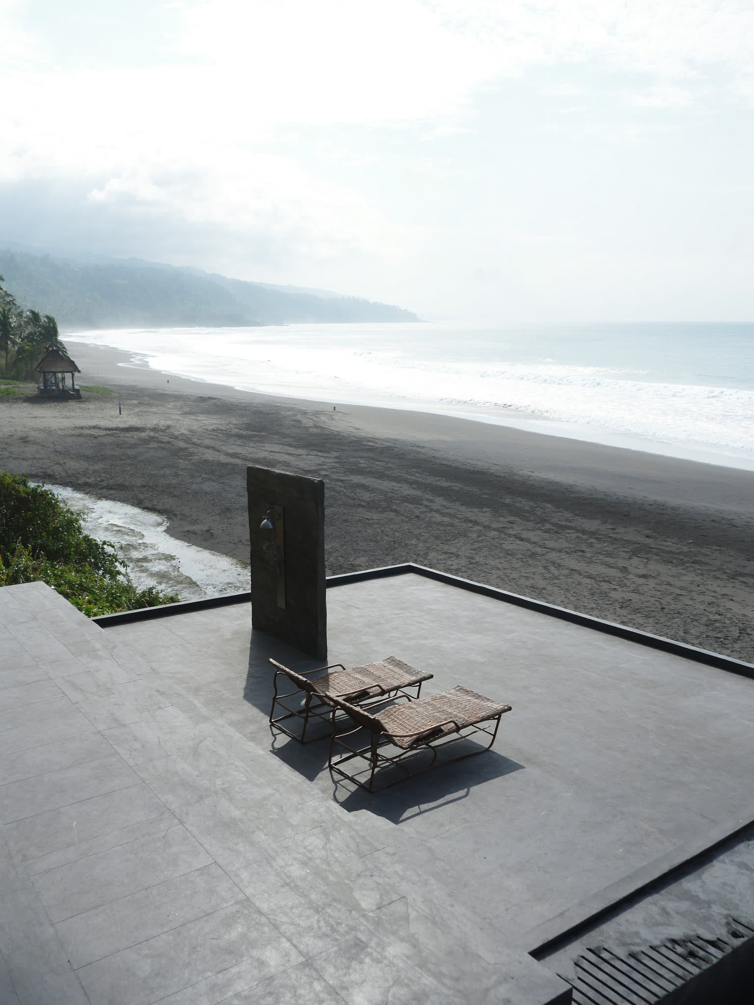 A stone terrace running to the edge of a black sand beach on the east coast of Bali.